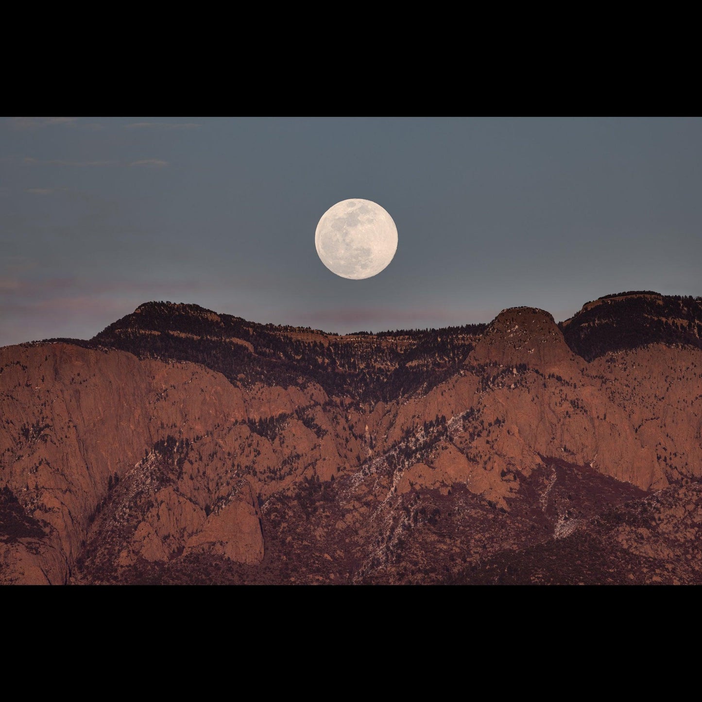 A full moon just after rising behind the Sandia Mountains.
